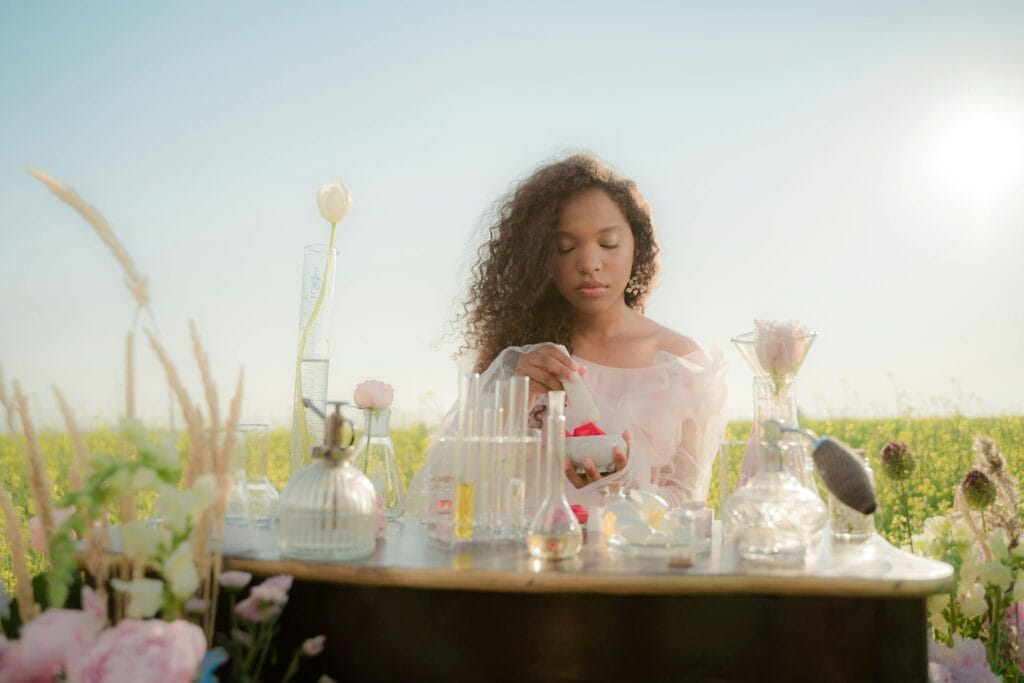 A young woman experimenting with perfumes at a table in a sunny meadow.
